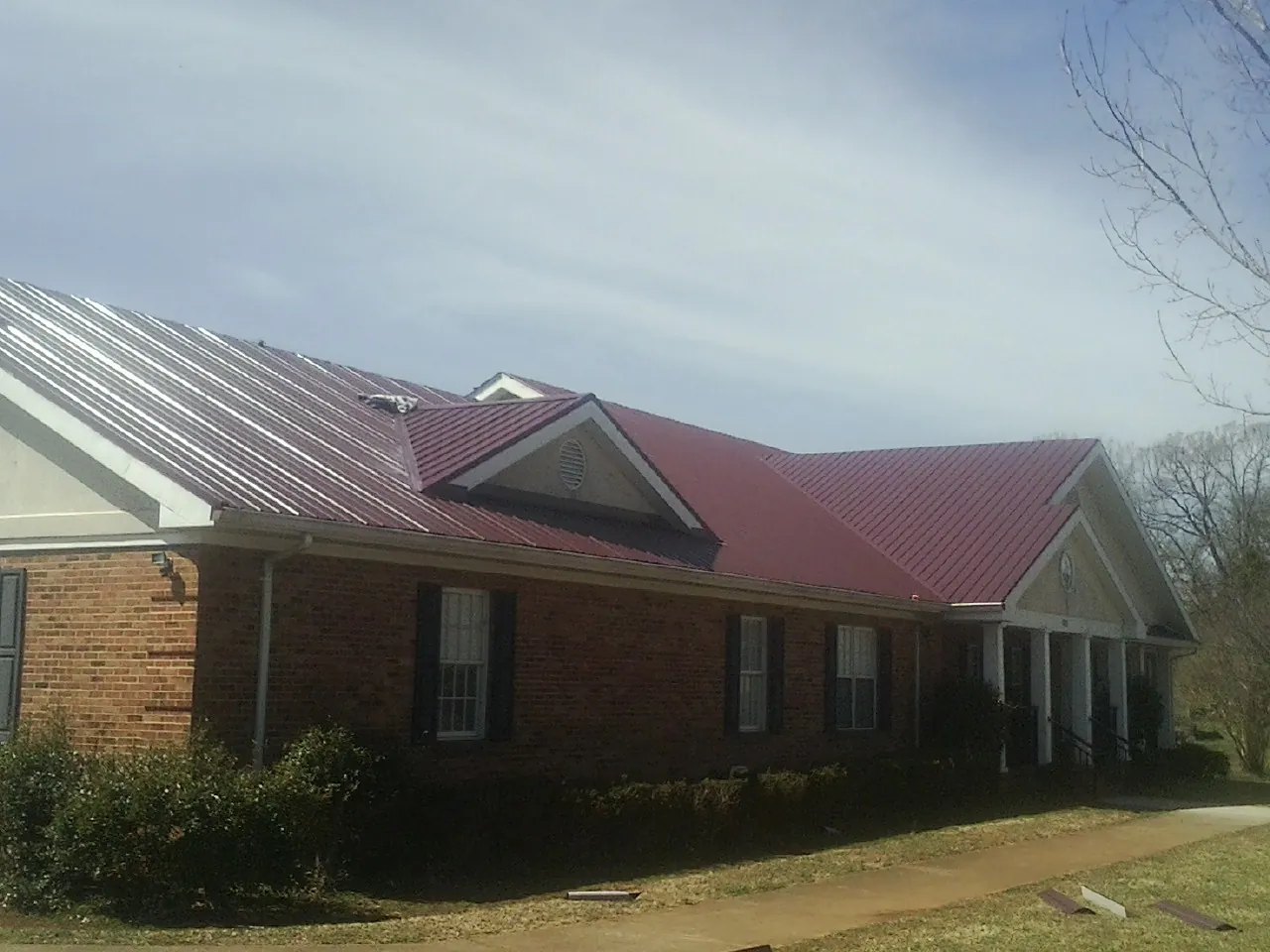 Red metal roof with gabled entries on a long brick building, from a Hail Damage Roof Repair job in Port Byron