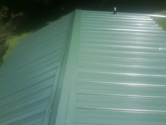 New green metal panels meeting at the ridge of a roof — Flat Roof Repair work by our crew in Port Byron