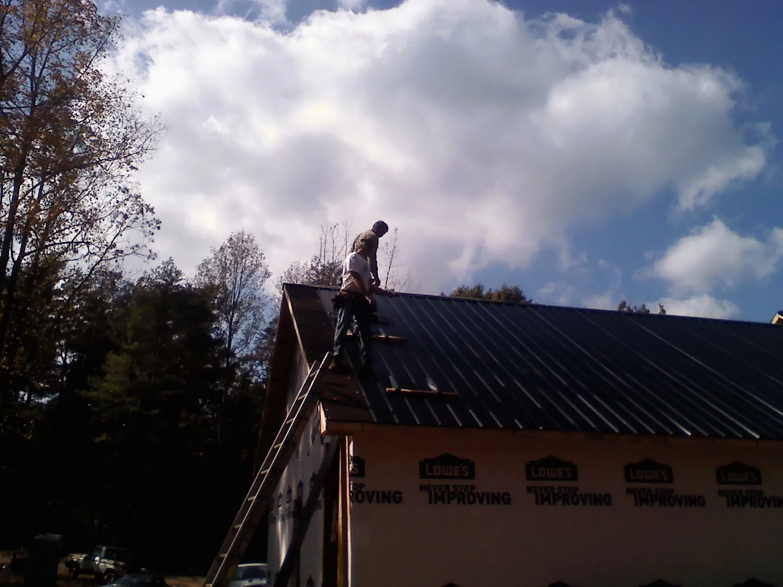 Roofer fastening dark metal panels high against a cloudy sky, from a Roof Inspection job in Port Byron