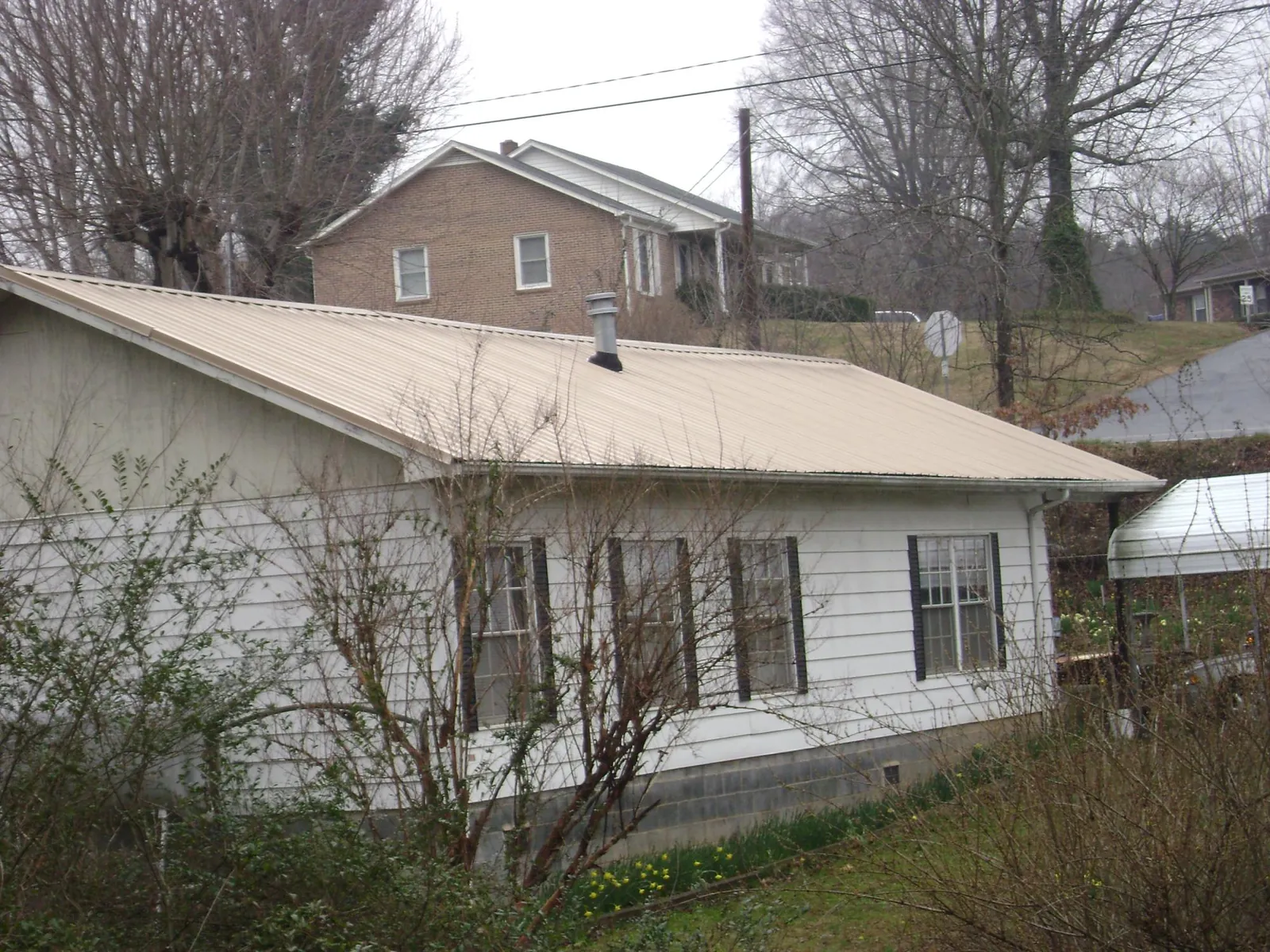 Tan metal roof on a white sided house set into a hillside — Commercial Roofing by Roofing Brothers in Port Byron
