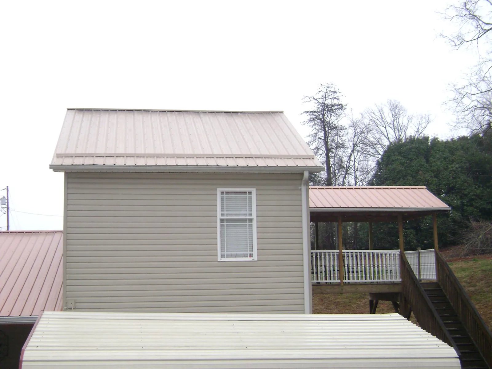 Tan metal roofs on a two story addition and attached porch, from a Roof Replacement job in Port Byron